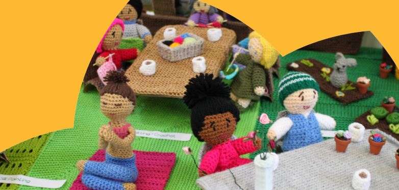 Knitted puppets sat together at table doing arts and crafts