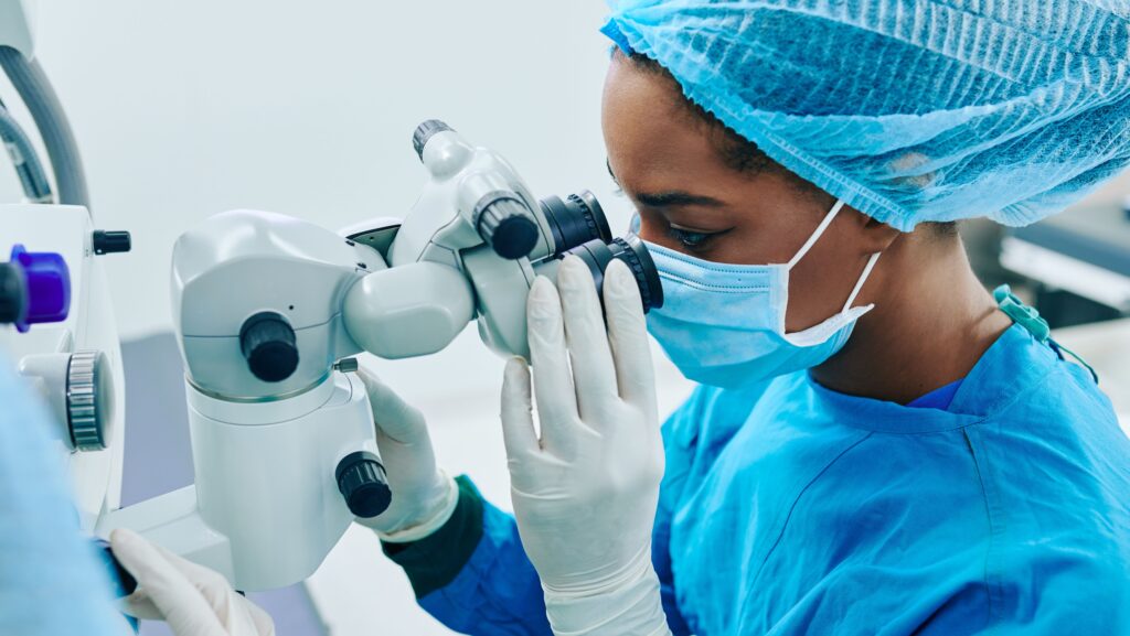 Eye doctor looking through microscope with medical scrubs on