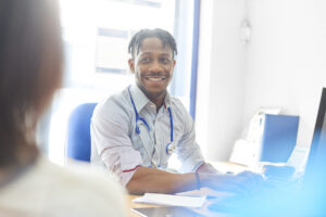 Smiling doctor typing out prescription for patient on computer